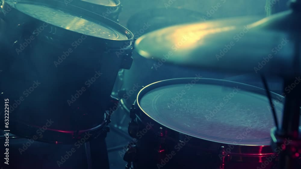 A drummer plays on a dark stage in the fog and neon lights.