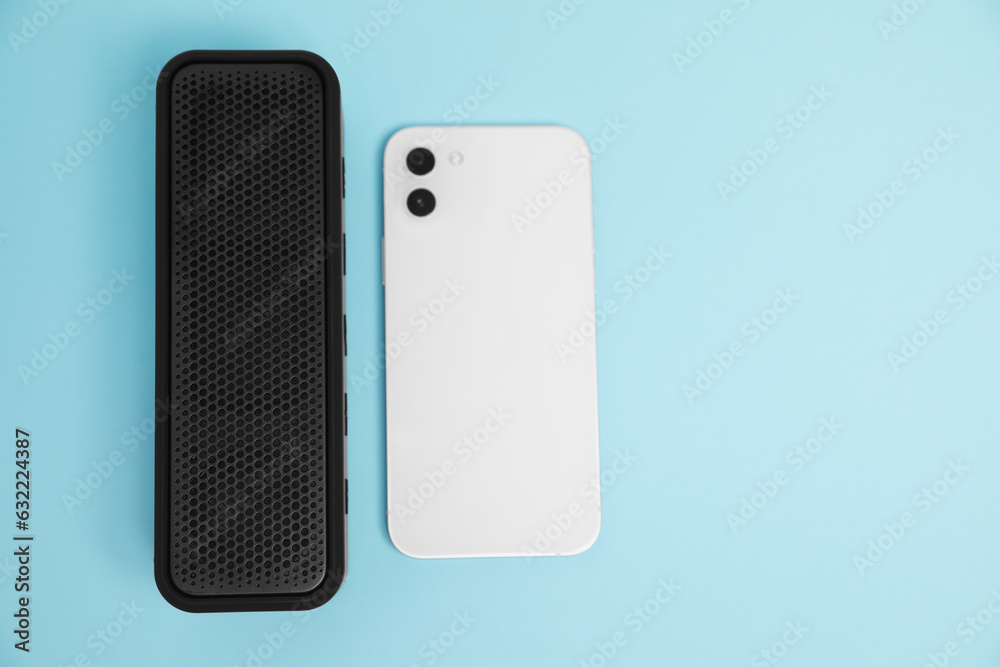 Portable bluetooth speaker and smartphone on light blue background, flat lay with space for text. Audio equipment Portable bluetooth speaker and smartphone on light blue background, flat lay with space for text. Audio equipment
