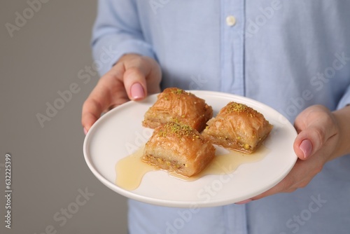 Woman with plate of delicious sweet baklava on grey background, closeup