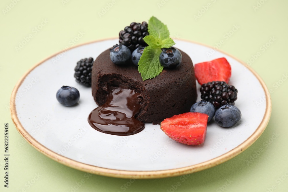 Plate with delicious chocolate fondant, berries and mint on light green table, closeup Plate with delicious chocolate fondant, berries and mint on light green table, closeup