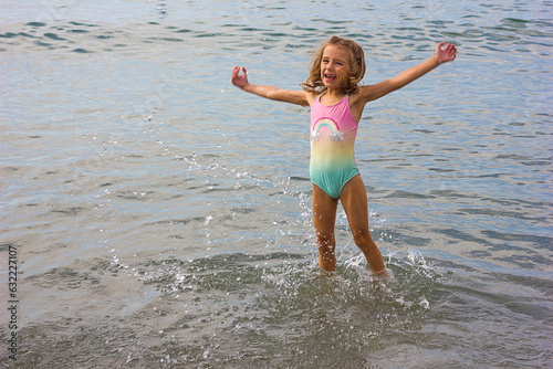 Beautiful happy little girl playing in the waves and splashes on the sea	