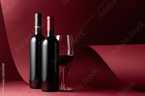 Bottles and glass of red wine on a red background.