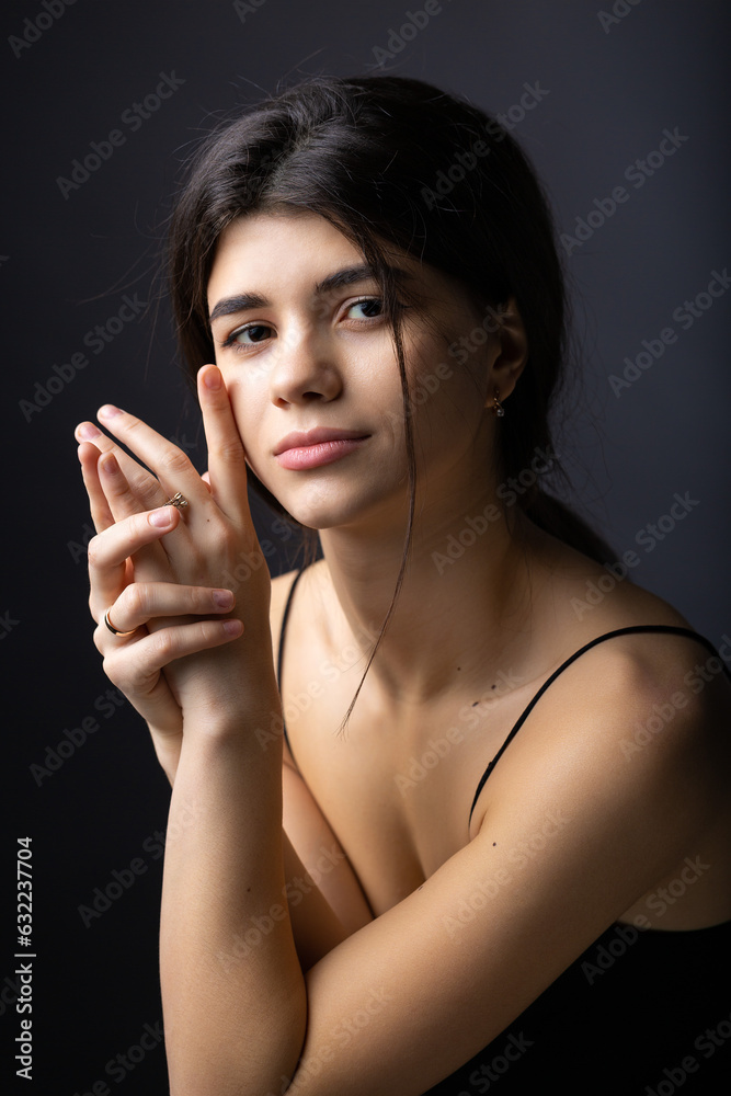 Classic studio portrait of a young brunette dressed in a black top, who is sitting on a chair against a black background. Classic studio portrait of a young brunette dressed in a black top, who is sitting on a chair against a black background.