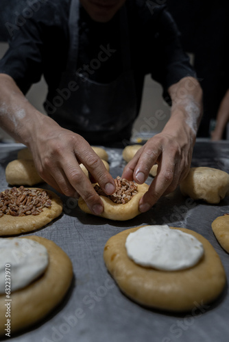 A young Hispanic baker is stuffing dough buns with nuts