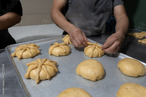 A young Hispanic baker is placing dough bones to prepare day of the dead bread