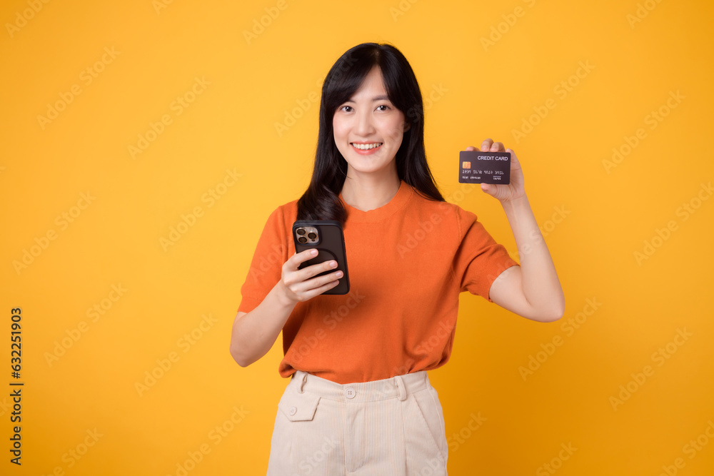 Vibrant young Asian woman in her 30s, using smartphone and holding credit card on yellow background. Convenient online shopping. Vibrant young Asian woman in her 30s, using smartphone and holding credit card on yellow background. Convenient online shopping.