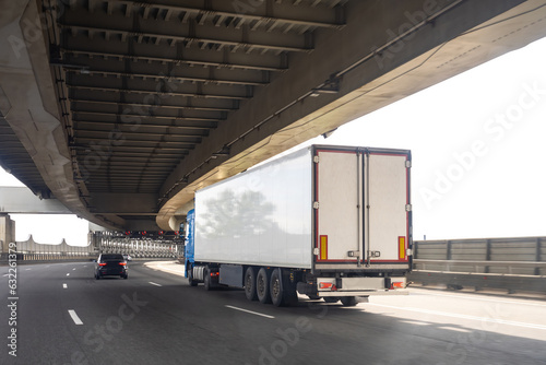 White truck under overpass. Lorry is driving along road. Freight logistics transportation. White truck at road junction. Transport for importing goods. Lorry on two-level bridge. Truck business