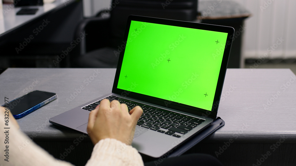 Over the shoulder shot of a business woman working in office interior on pc on desk, looking at green screen. Office person using laptop computer with laptop green screen, sitting at wooden table Over the shoulder shot of a business woman working in office interior on pc on desk, looking at green screen. Office person using laptop computer with laptop green screen, sitting at wooden table