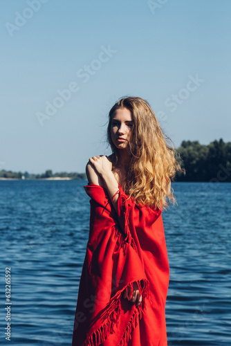 Woman wrapped in red plaid standing near the sea in sunny day. Concept fashion photo. 