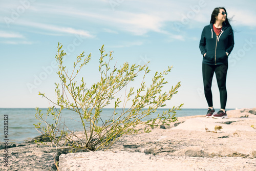 plant on the beach with the ocean in the background and a woman in sportswear looking to the side