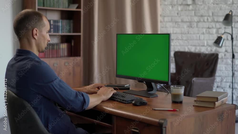 Young Man Working at His Desk Using Computer with Green Mock-up Screen, Chroma Key Display. Working from Cozy Home Office, Studio Young Man Working at His Desk Using Computer with Green Mock-up Screen, Chroma Key Display. Working from Cozy Home Office, Studio