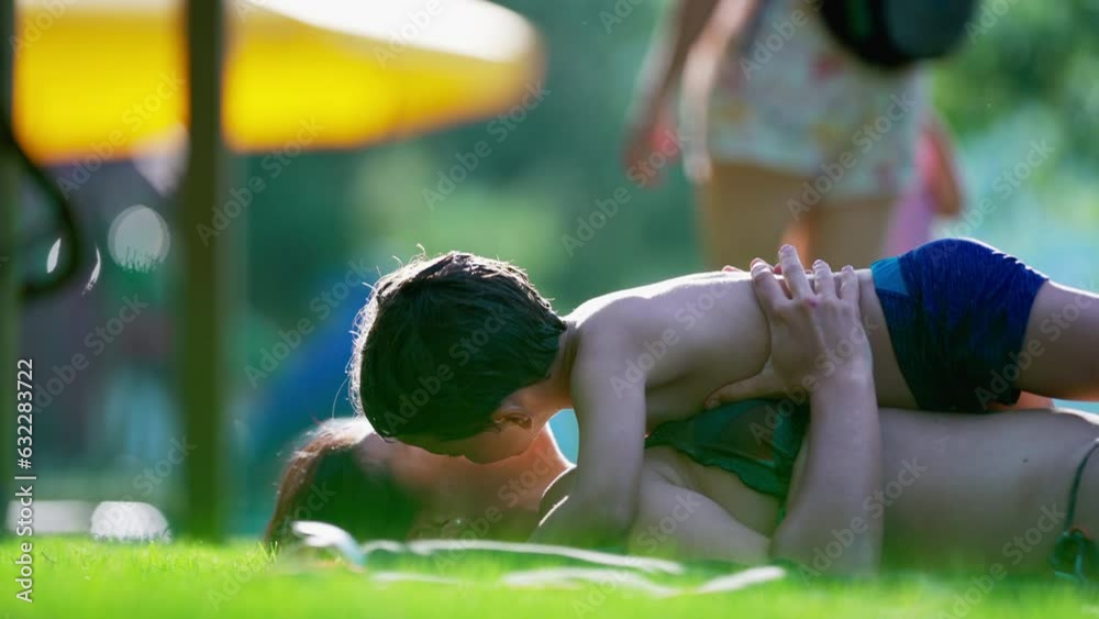 Candid loving moment between mother and child laid on grass during summer day activity, little boy wanting to kiss mom, authentic tender moment