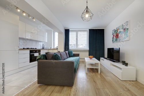 Nowoczesny apartament z zielona sofą, telewizorem i otwartą kuchnią photo
