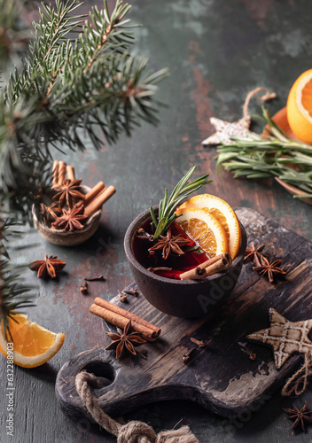 Mulled wine in brown ceramic mug with orange slices and spices. Christmas hot drink on wooden table with xmas tree branches, festive card