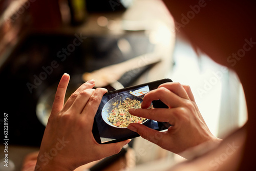 Young woman using a smart phone to take a photo of a meal she is cooking and preparing in the kitchen