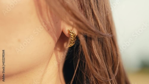 Young woman with gold wheatear earrings posing outdoors. Jewelry details photo