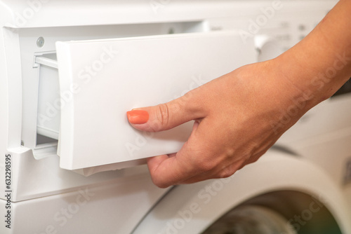 A woman opens the tray for pouring laundry detergent into the washing machine. The concept of washing dirty clothes in a washing machine. Use of various detergents for clothes.