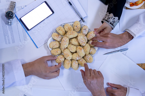 Arabic working colleagues hands  eating eid kahk together on working desk photo