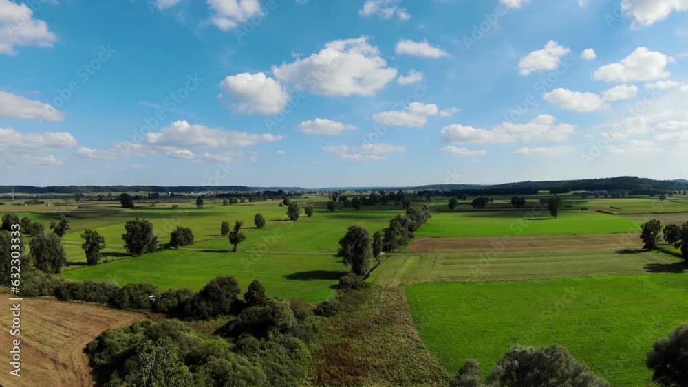 Flug mit der Drohne über eine Kulturlandschaft in Süddeutschland mit grünen Feldern, Bäumen und Sträuchern. Die Felder sind eine Mischung aus Grün und Braun mit einigen Anbauflächen. Der Himmel ist he