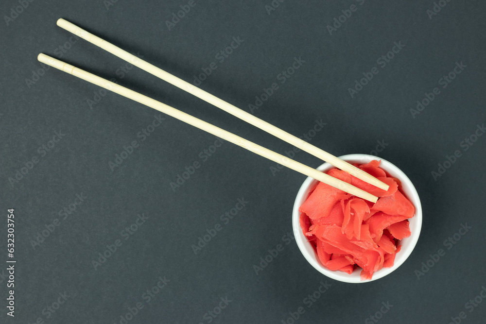White bowl with pickled ginger and wooden chopsticks. Component for serving sushi on black surface. Top view, flat lay, space for text. White bowl with pickled ginger and wooden chopsticks. Component for serving sushi on black surface. Top view, flat lay, space for text.