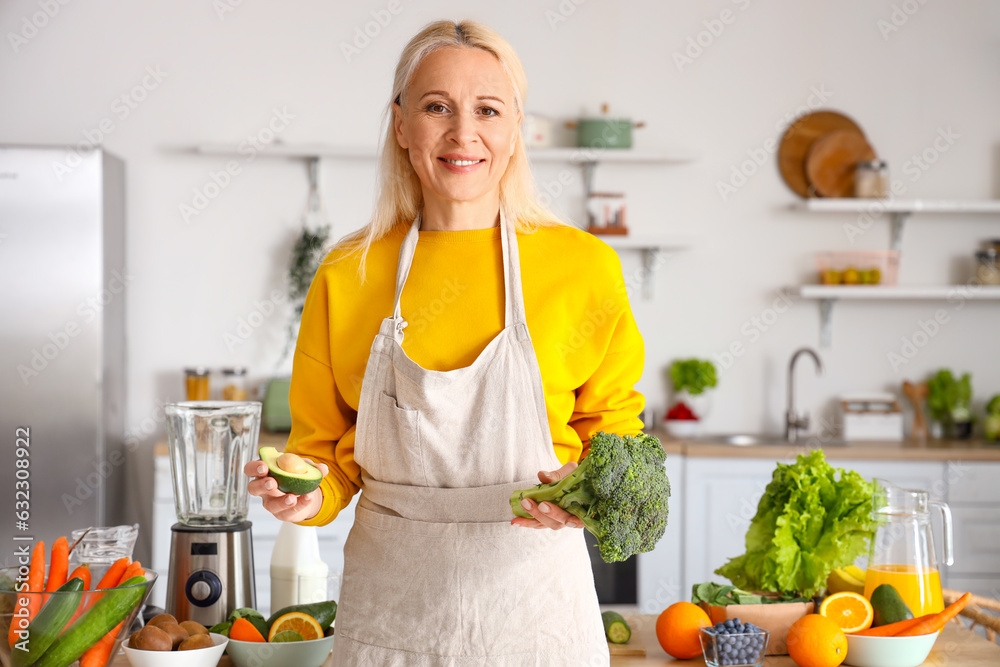 Mature woman with avocado and broccoli making healthy smoothie in kitchen