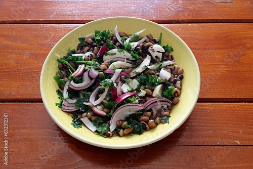 Black-eyed peas salad dish with onions, parsley, and olive oil, on a plate on a wooden table. Selective focus