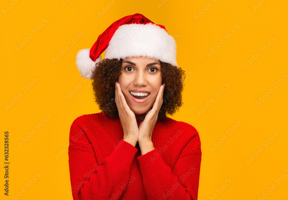 Surprised cheerful young African American woman in santa claus and knitted red sweater on yellow background, looking at the camera and smiling. Big christmas discounts, sale concept Surprised cheerful young African American woman in santa claus and knitted red sweater on yellow background, looking at the camera and smiling. Big christmas discounts, sale concept