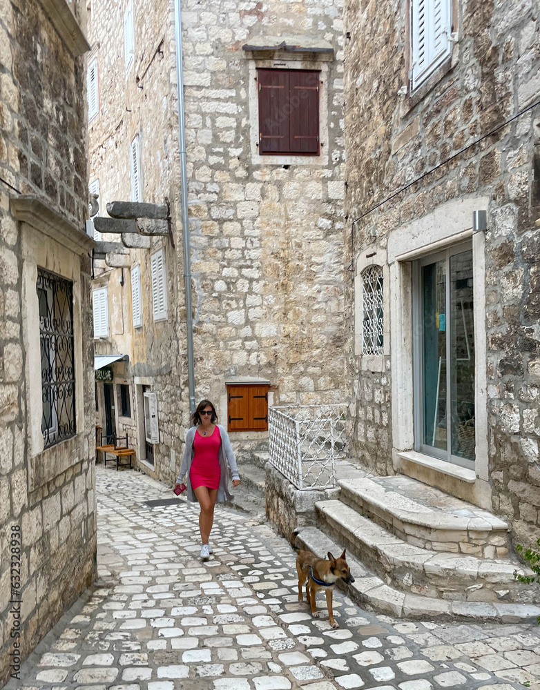 Pretty tourist is exploring picturesque old streets of island town with her dog