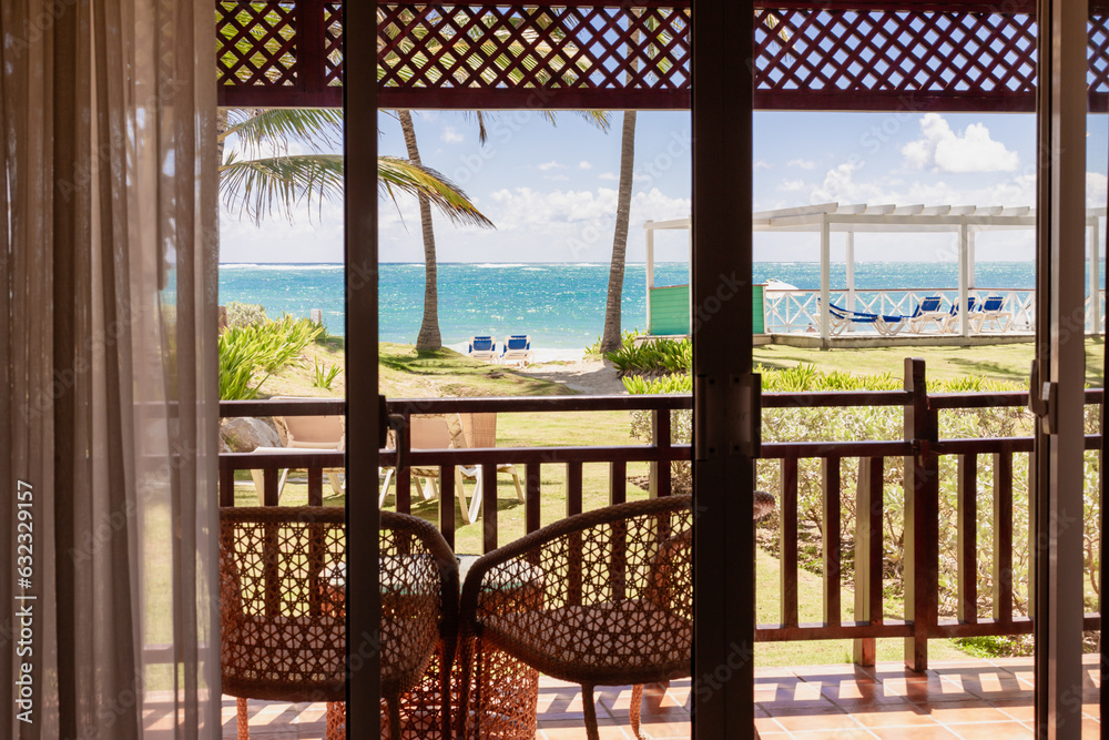 vue sur un balcon avec des chaises extérieur avec vue sur la mer turquoise et un palmier lors d'une journée ensoleillée