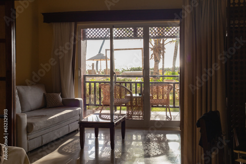 vue sur un balcon avec des chaises extérieur avec vue sur la mer et un palmier lors d'une journée ensoleillée à partir de l'intérieur d'une pièce