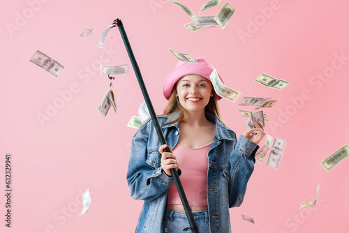 Happy young woman with fishing rod and money on pink background photo