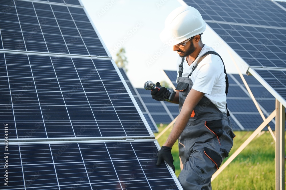 Male arabian engineer in helmet and brown overalls checking resistance in solar panels outdoors. Indian man working on station. Male arabian engineer in helmet and brown overalls checking resistance in solar panels outdoors. Indian man working on station.
