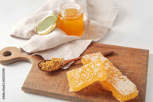 Jar of delicious honey, combs and bee pollen on light background