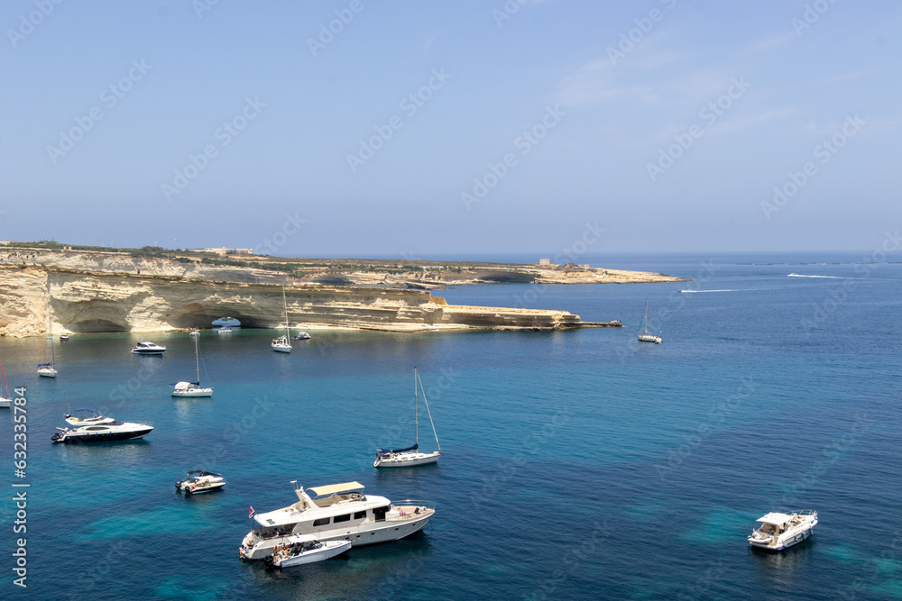 View on the beach, cliffs and yachts, ships and motorboats by Il-Ħofra l-Kbira Bay in Malta