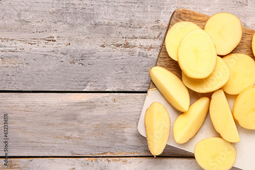 Board with slices of fresh raw potatoes on grey wooden background