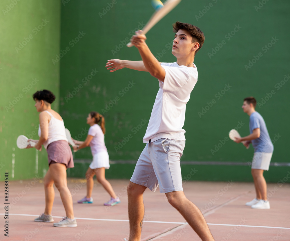 Young male pelota player hitting ball with wooden racket during training game on outdoor Basque pelota fronton.