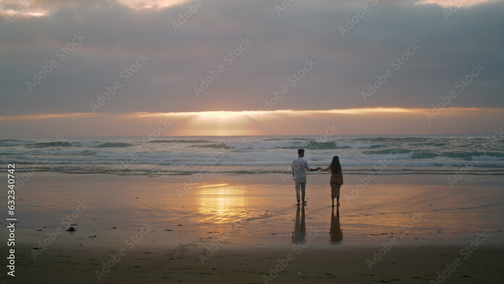 Affectionate newlyweds going sunrise sea shore. Loving woman holding man hand