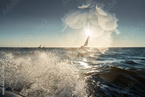 The view through the spray of how the sailboat is heeling at sunset, splashes shine in the sun, sailors are on the board