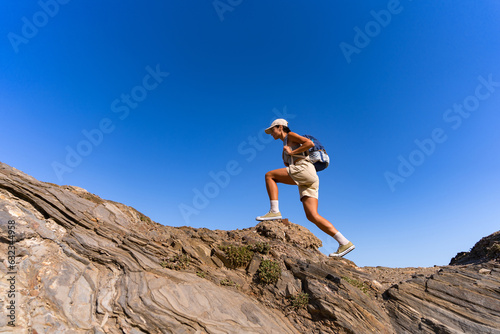 tourist girl with a backpack on her back climbs the mountain in summer