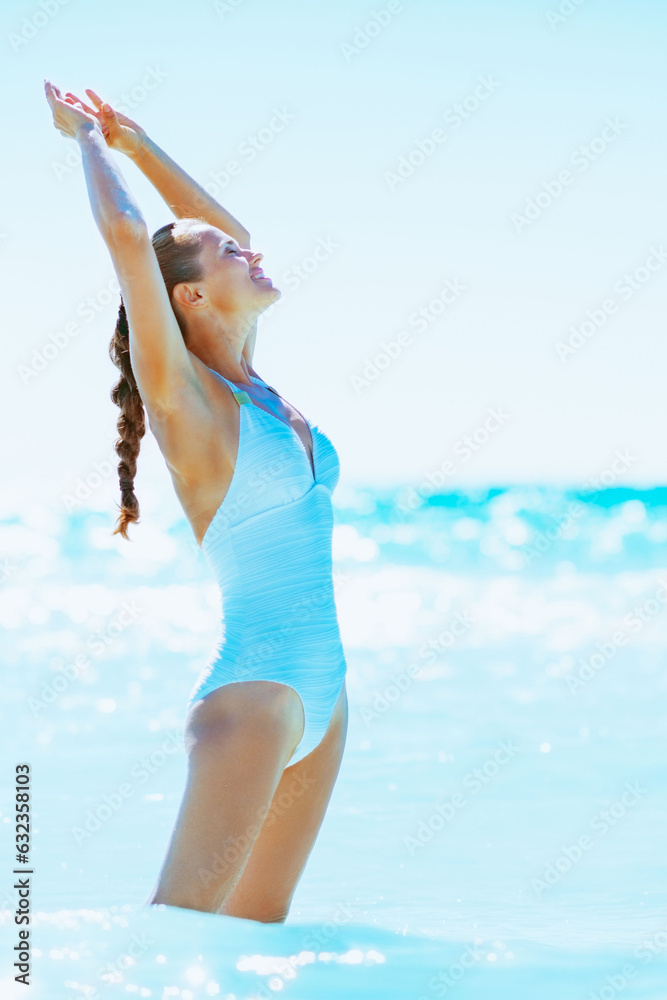 Happy young woman standing in sea and rejoicing