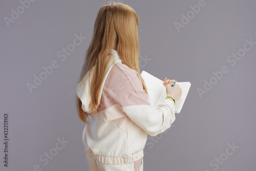 Seen from behind teen girl in beige tracksuit writing