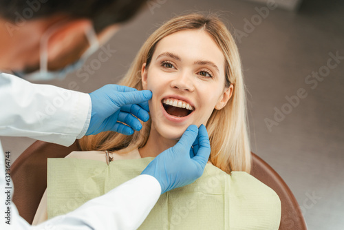 Young female patient with blond hair sitting in dental chair with open mouth  dentist checking teeth
