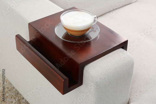 Cup of coffee on sofa with wooden armrest table indoors. Interior element photo