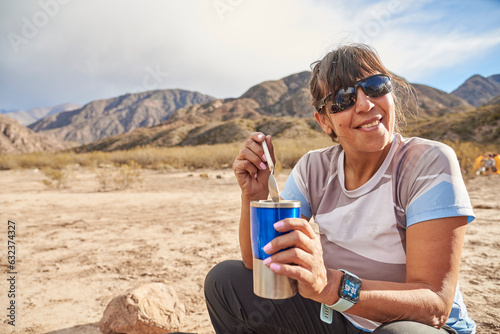 Happy latin woman having a hot drink for breakfast at mountain camp, a sunny morning. Composition with copy space.