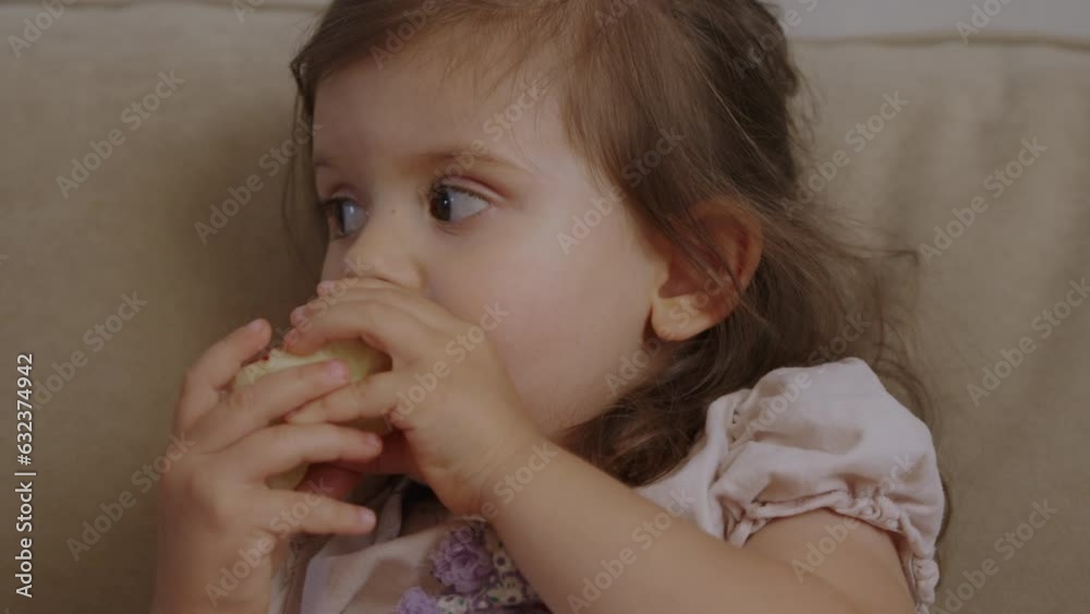 Little girl eating apple sitting on sofa at home. Healthy eating. Healthy food, diet. Organic food. Delicious food. Little girl eating apple sitting on sofa at home. Healthy eating. Healthy food, diet. Organic food. Delicious food.