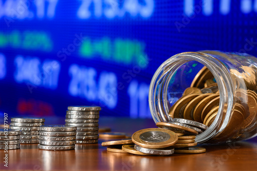 The coins fall out of a glass jar, with a pile of coins on a financial market chart in the background. photo