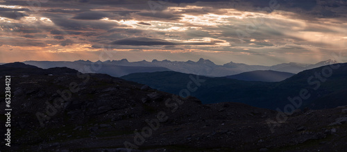 Panorama of dramatic high contrast sunset over the peaks from Rabothytta, Okstindan, Hemnes, Helgeland, Nordnorge. Norway dusk. Norwegian mountains at summer night. Light rays through clouds mountain