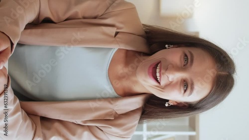 Vertical video. Online communication. Sincere joy. Therapy support. Emotional surprised smiling woman in business suit gesticulating laughing expressing emotions in light interior. photo
