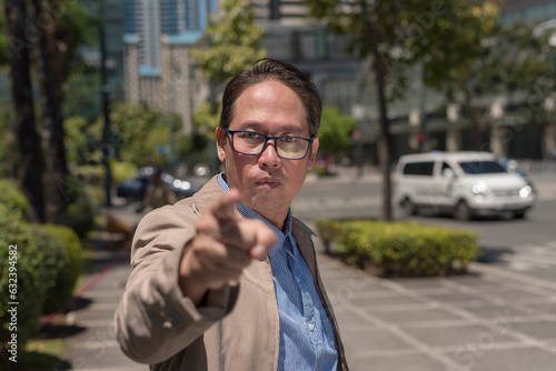 A self righteous and nosy asian man warns someone to back off. Pointing with his finger, looking furious. Outdoor city scene.