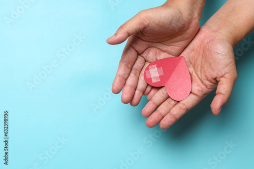 Hands hold of paper heart on blue background. Awareness of World Hemophilia Day, World AIDS and HIV Day. 